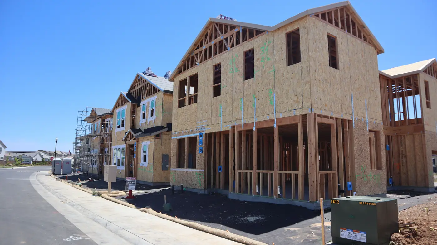 A row of new two-story houses along a street, sheathed and framed, at different stages of construction.